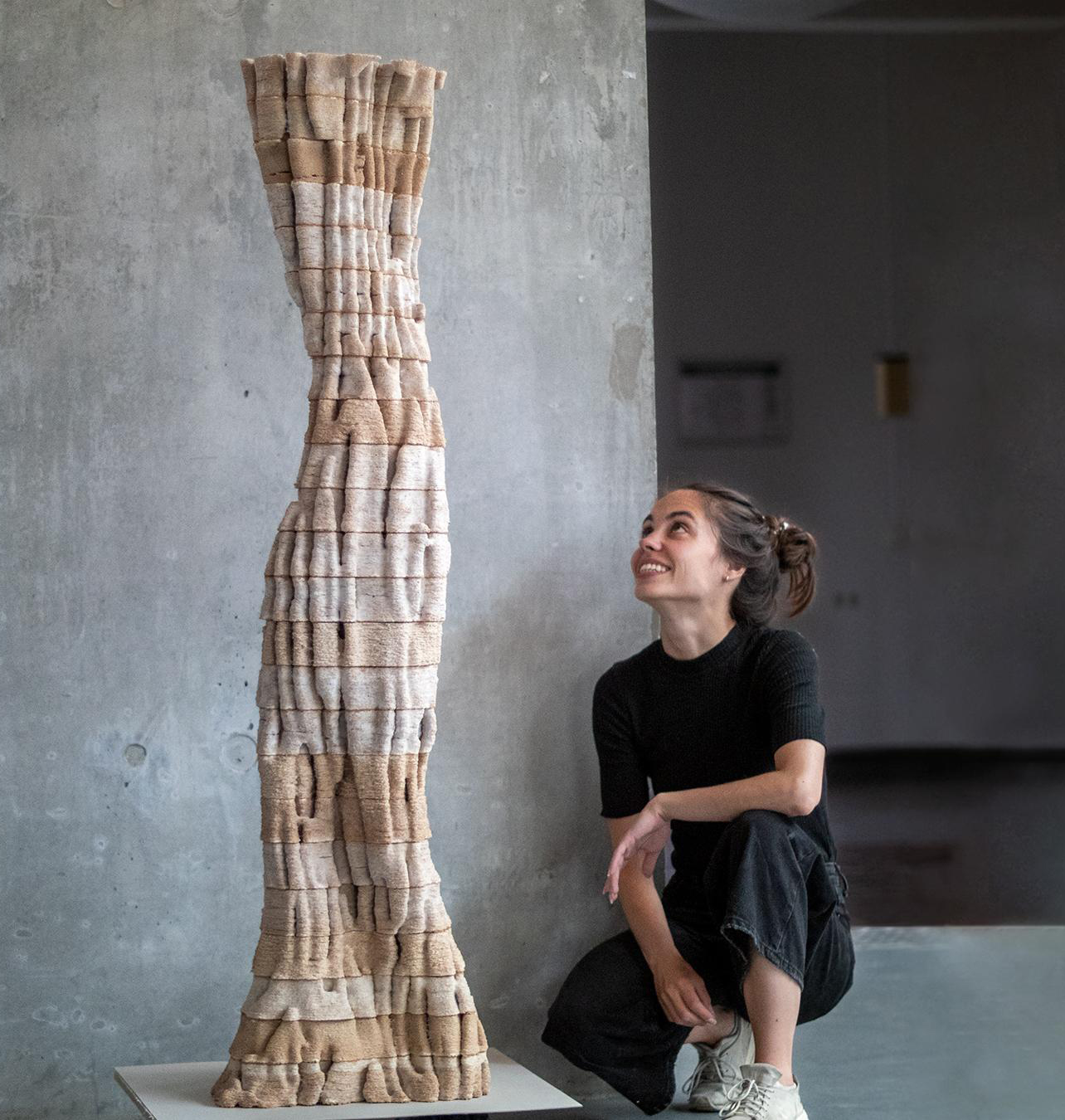 Ana Goidea sits on the floor and looks up at the sculpture they created for the project. Photo.